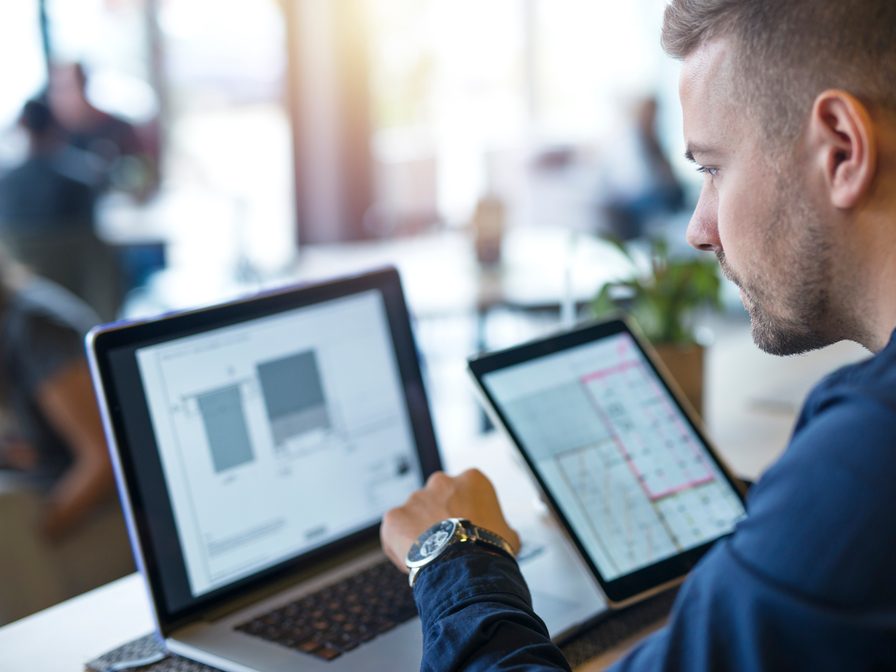 Entwickler am Schreibtisch vergleicht einen Entwurf auf Laptop und Tablet