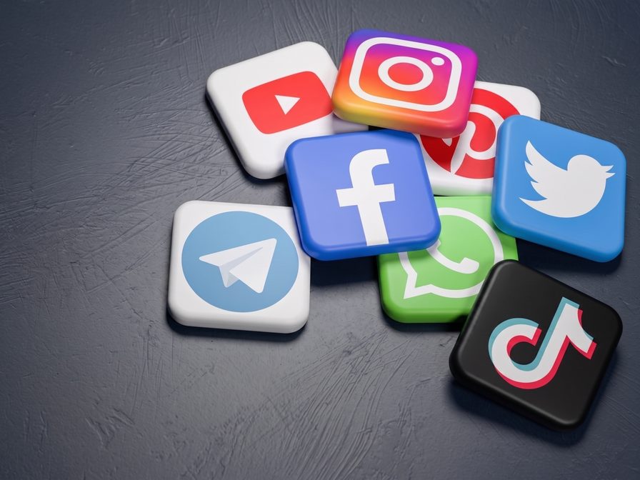 Dreidimensionale App-Symbole von Instagram, Facebook, TikTok, YouTube und WhatsApp auf dunklem Stein