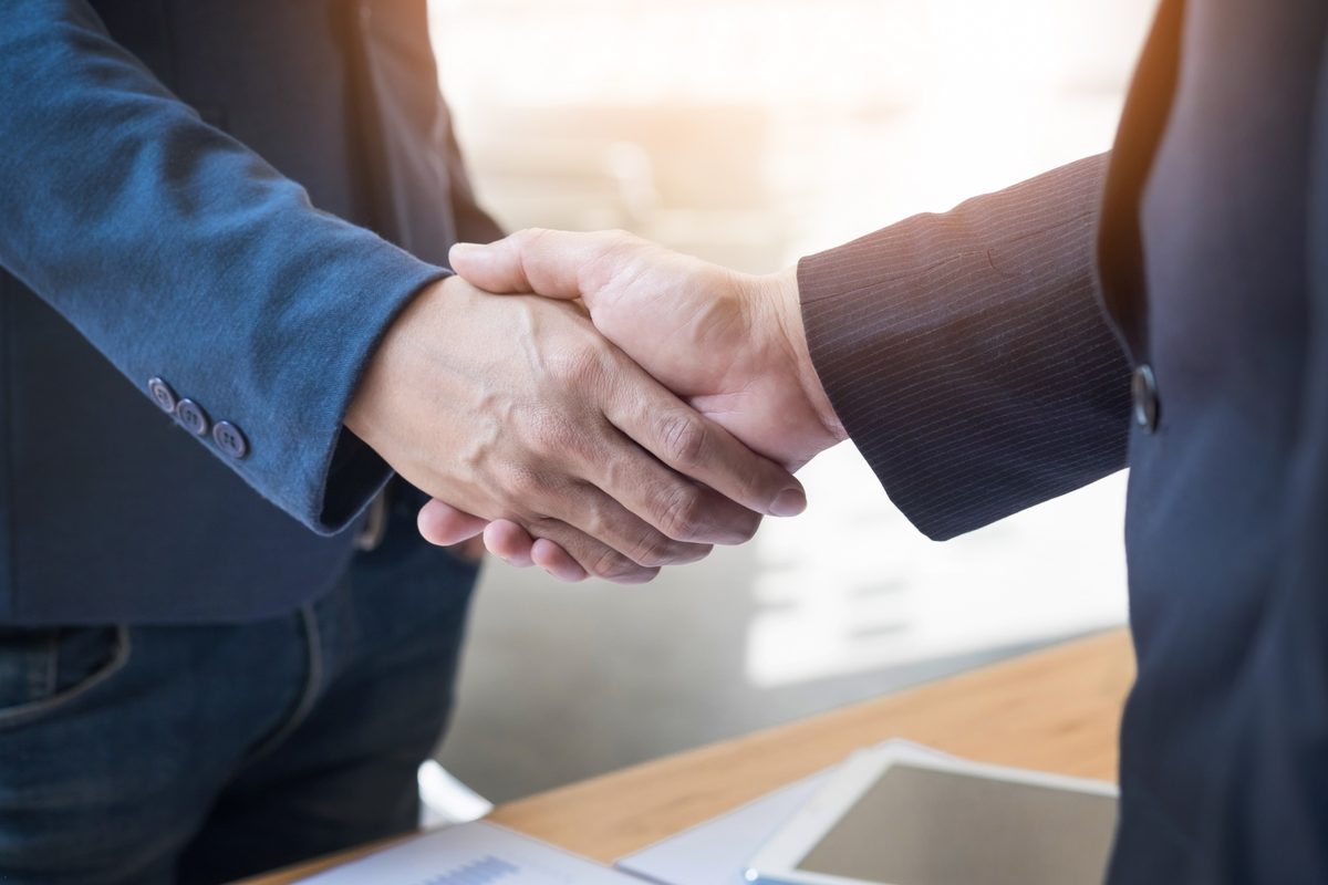 Zwei Personen in Businesskleidung geben sich über einem Schreibtisch die Hand